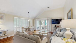 A spacious living room with a sofa, coffee table, and TV. There is a dining area with chairs and a table. - Condo with sunset views, with ocean/inlet views - walk to the Beach Club (Seabrook Island)