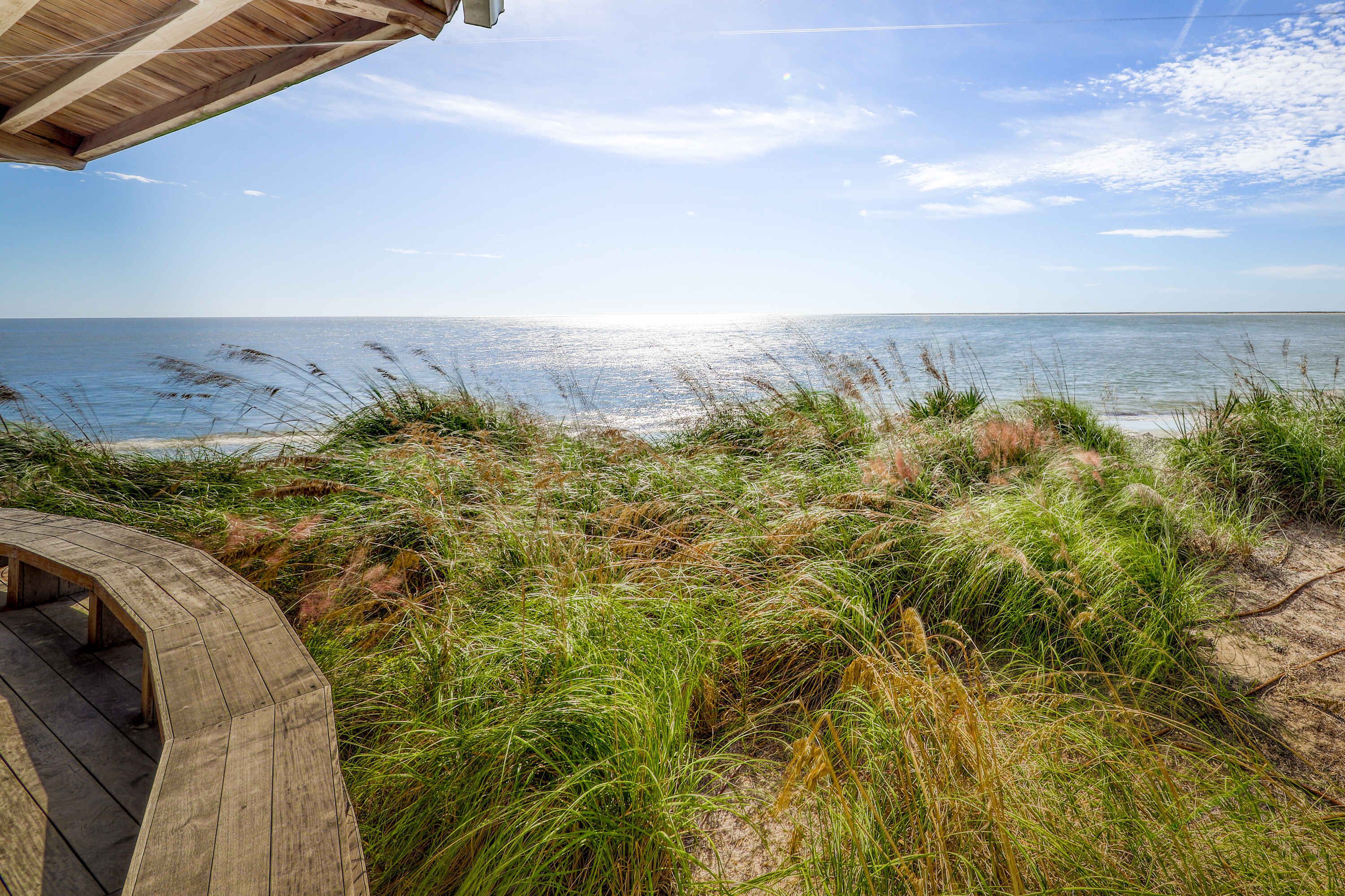 A wooden deck overlooking a beach with grassy dunes and the ocean.