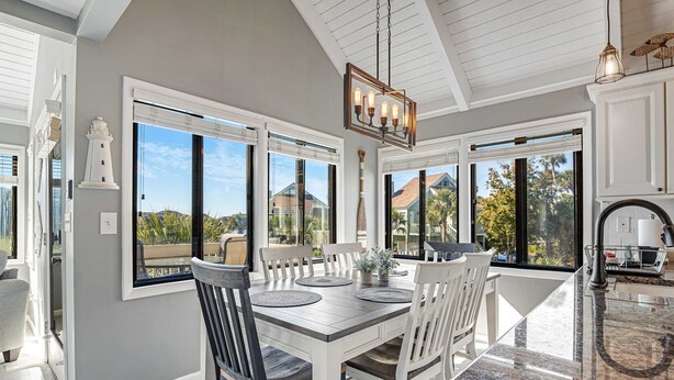 Un comedor con mesa y sillas blancas, ventanas amplias y vistas al exterior.