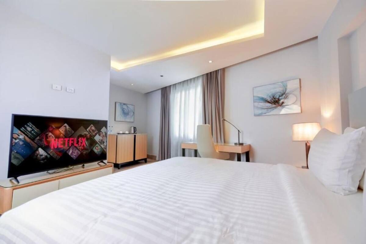 A hotel room with a large bed, a desk, a chair, a television, and a lamp.