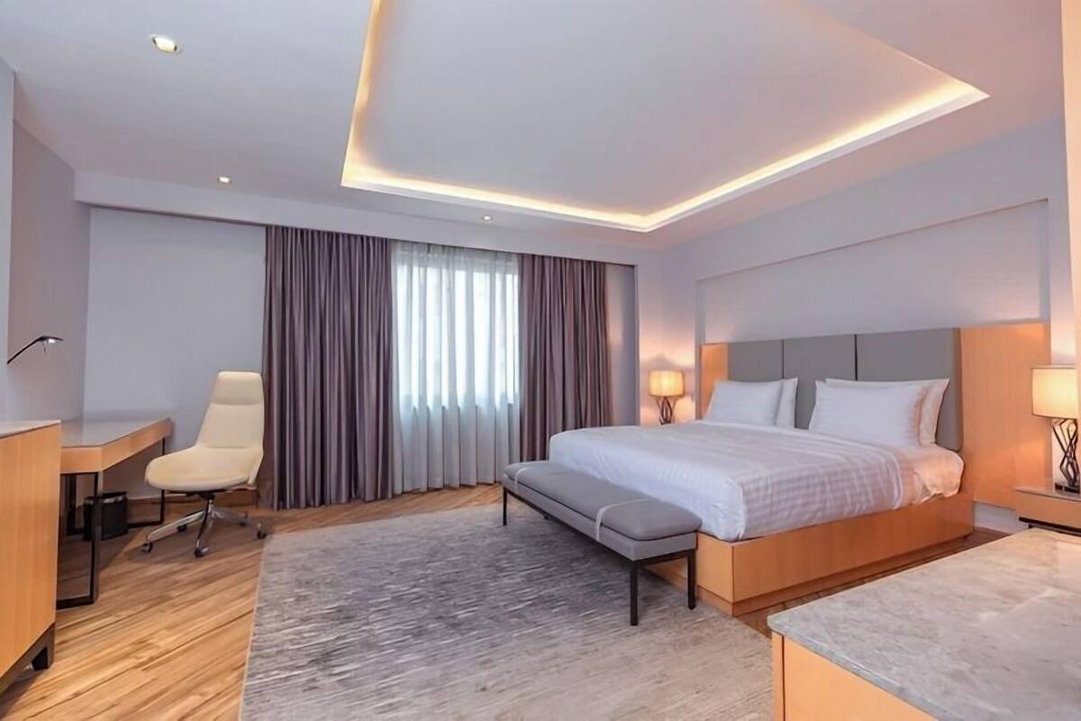 A modern hotel room with a large bed, a desk, a chair, and a small table.