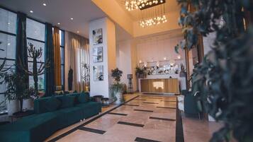 A spacious lobby with a green sofa, potted plants, and a reception desk.
