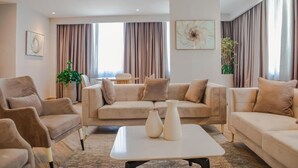 Ein modernes Wohnzimmer mit einem beigefarbenen Sofagarnitur, einem Couchtisch mit Vasen und einem großen Fenster mit Vorhängen.