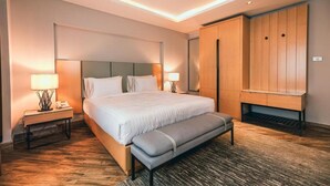 Una habitación de hotel moderna con una cama grande, lámparas de noche, un banco y un armario de madera.