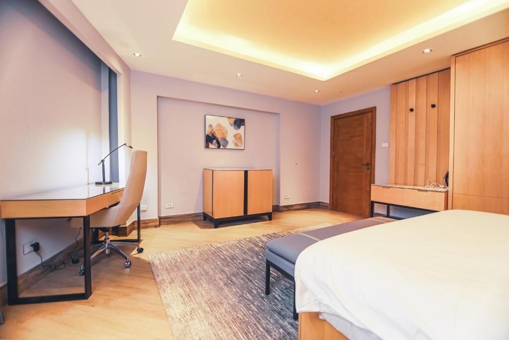 A modern bedroom with a desk, chair, bed, wardrobe, and a painting on the wall.