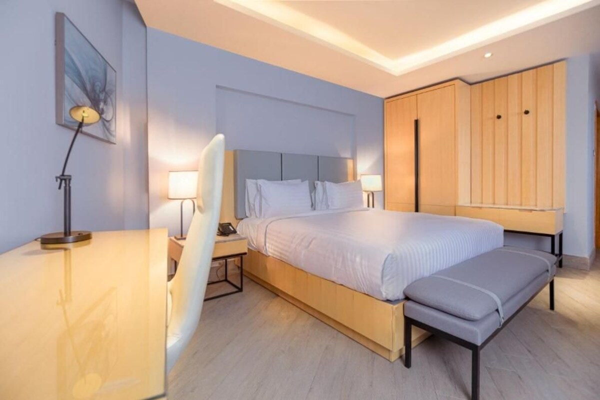 A modern hotel room with a bed, bedside tables, a desk, and a wardrobe.