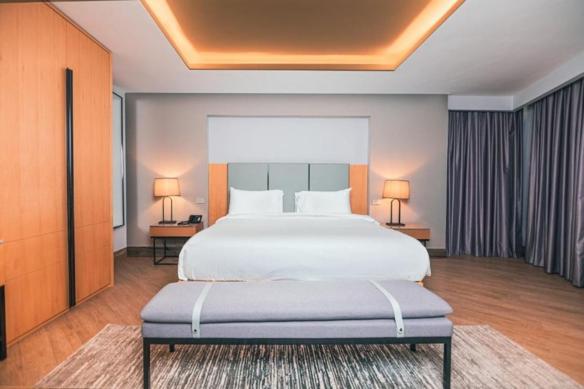 Una habitación de hotel moderna con una cama grande, lámparas de noche, un banco y un armario de madera.