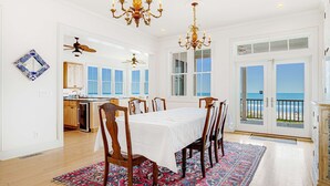 A dining area with a table set for six, a patterned rug, and a view of the ocean through large windows. - Gorgeous Beachfront Home w/ Oceanfront Views, Deck, Beach Boardwalk & WiFi (Folly Beach)