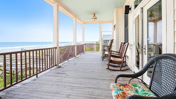 A wooden deck with a railing overlooking the ocean, a rocking chair, and a wicker chair. - Gorgeous Beachfront Home w/ Oceanfront Views, Deck, Beach Boardwalk & WiFi (Folly Beach)