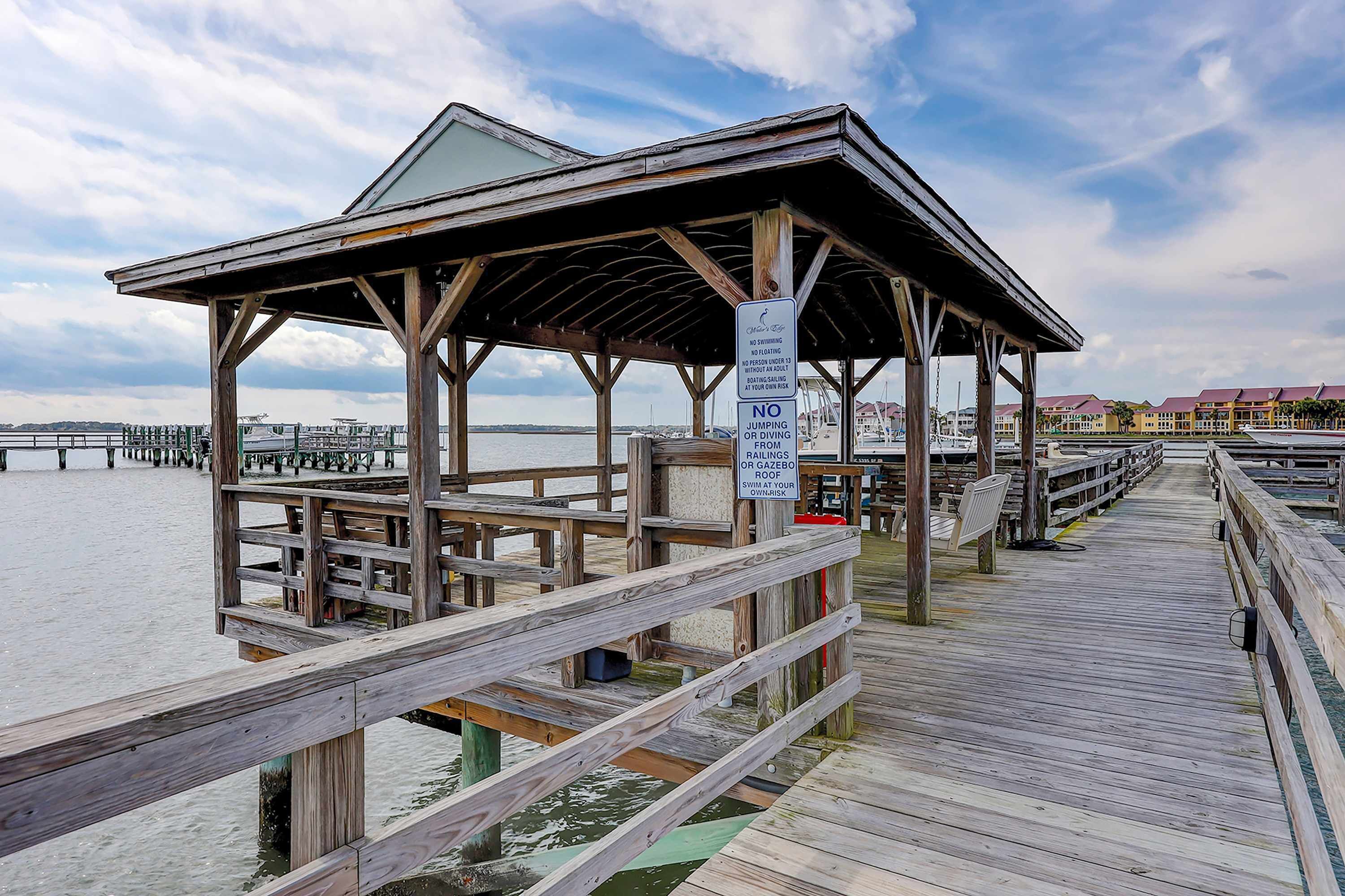 A wooden pier with a covered seating area and a sign prohibiting swimming or diving.