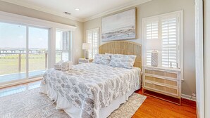 Ein Schlafzimmer mit einem großen Bett, Blick ins Freie, Deckenventilator und Nachttisch mit Lampe.