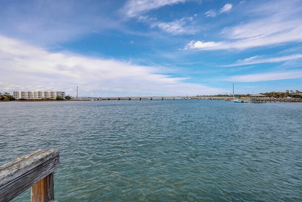 A waterfront view with a wooden dock, a bridge, and a building in the background.