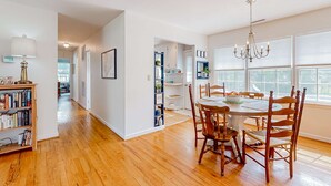 Une salle à manger spacieuse, avec une table et des chaises en bois, un lustre et une bibliothèque remplie de livres.