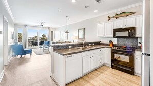 Una cocina moderna con armarios blancos, encimera de granito, refrigerador de acero inoxidable y una decoración con forma de pez en la pared.