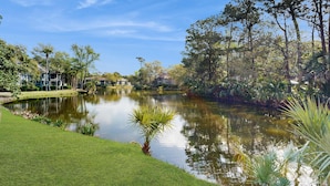 A serene lakeside view with a well-maintained lawn, a small pond, and surrounding trees.