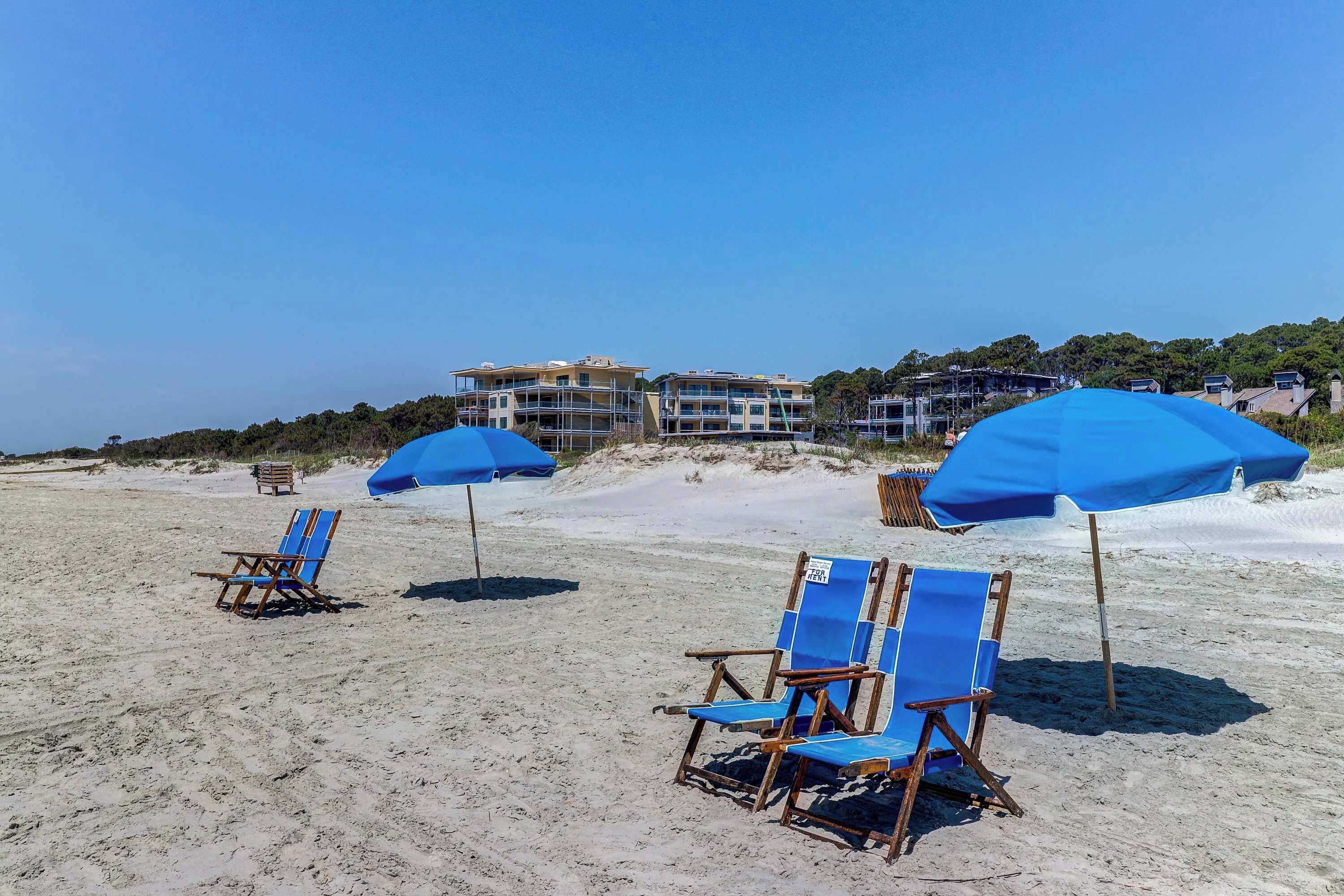 A beach with blue umbrellas and beach chairs.