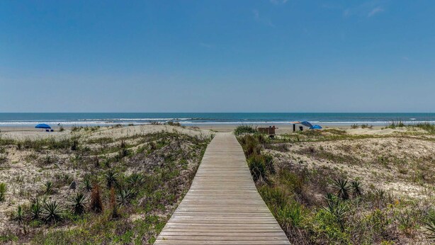 A wooden boardwalk leading to a beach with dunes and sparse vegetation.