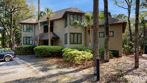 A two-story house with a sloped roof, surrounded by trees and bushes.