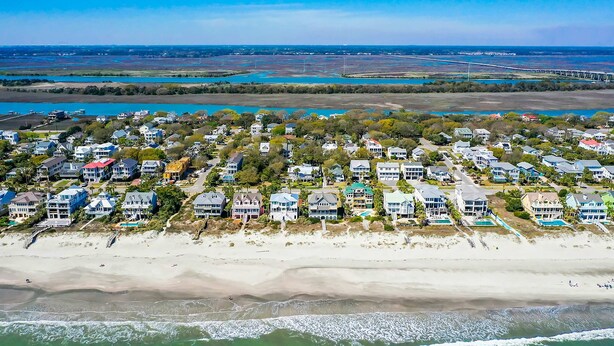 An aerial view of a coastal residential area with houses along the beach, a bridge in the distance, and a clear blue sky. - Gorgeous home with private pool, deck, enclosed patio, central AC, & balcony (Isle of Palms)