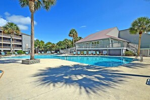 A swimming pool area with lounge chairs, palm trees, and a building with a balcony.