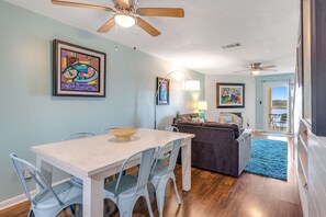 A dining area with a white table and chairs, a ceiling fan, and artwork on the walls.