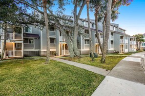 A row of two-story townhouses with balconies, a grassy lawn, and trees.