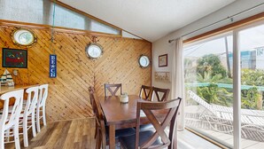 A dining area with a wooden herringbone wall, a wooden table with chairs, and a view of a pool and greenery outside.