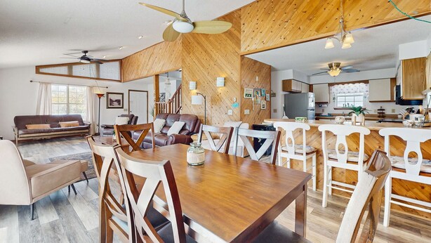 A spacious living room with a wooden dining table, chairs, and a ceiling fan.