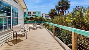 A wooden deck with lounge chairs and a railing, overlooking a garden with various plants and flowers.