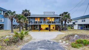 A two-story house with a balcony, palm trees, and a driveway leading to the entrance. - Beach Across the Street Ocean View Home w/ Roof Deck, Porch, AC - Dogs OK (Folly Beach)