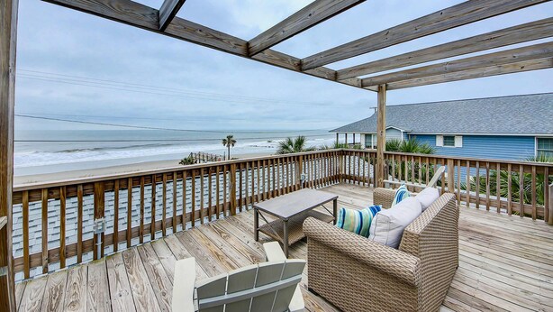 A wooden deck with a view of the beach, a wicker sofa, and a small table. - Beach Across the Street Ocean View Home w/ Roof Deck, Porch, AC - Dogs OK (Folly Beach)