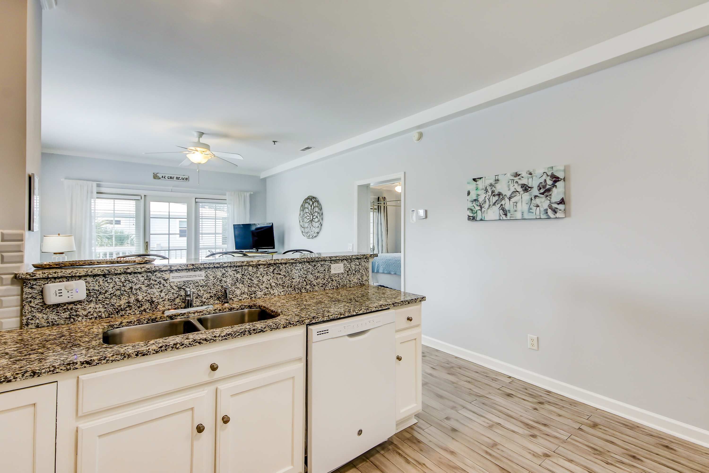 A modern kitchen with granite countertops, white cabinetry, and a dishwasher.