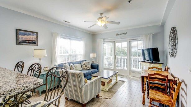 A spacious living room with a blue sofa, a dining table with chairs, a coffee table, and a ceiling fan. - Fantastic condo with water-view, pool, balcony, central AC, & washer/dryer (Folly Beach)