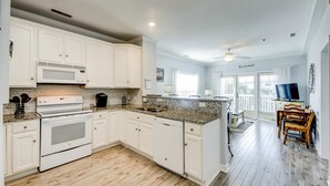 A kitchen with white cabinets, a microwave, an oven, and a dishwasher. There is a dining area with a table and chairs. - Fantastic condo with water-view, pool, balcony, central AC, & washer/dryer (Folly Beach)