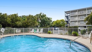 A swimming pool with a no lifeguard sign, surrounded by a fence, and adjacent to a multi-story building. - Fantastic condo with water-view, pool, balcony, central AC, & washer/dryer (Folly Beach)