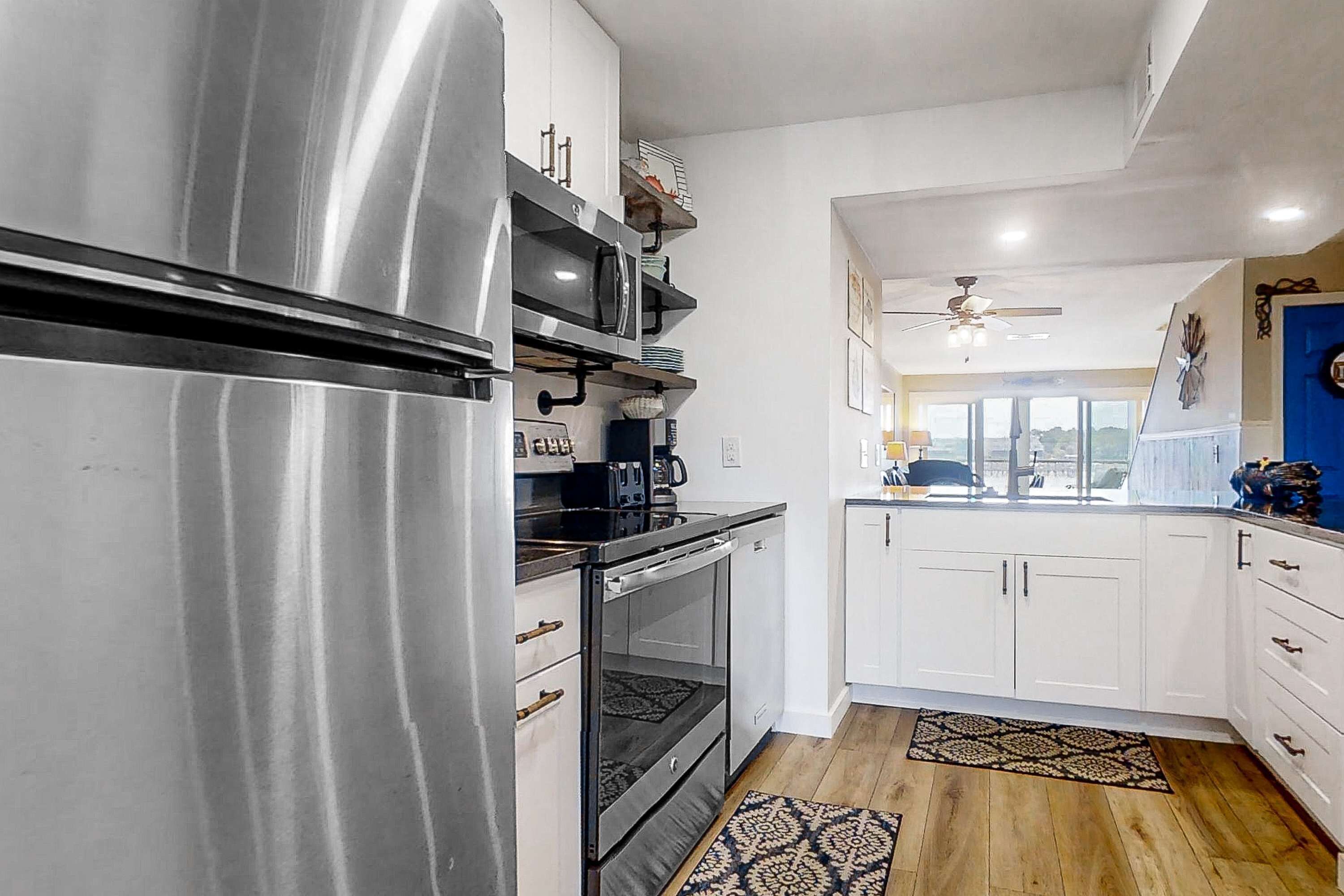 A modern kitchen with stainless steel appliances, white cabinetry, and a wooden floor.