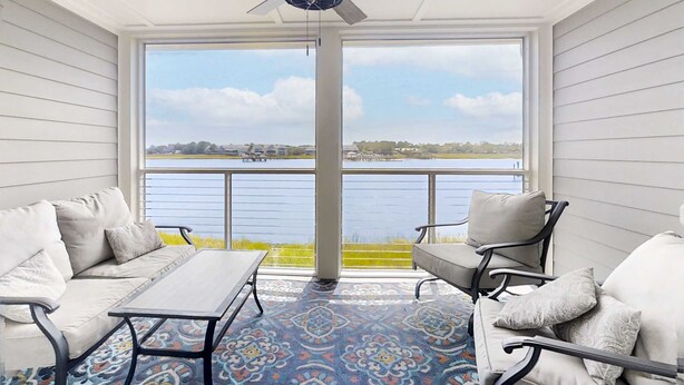 A covered balcony with a view of a lake, furnished with a sofa, chairs, and a table. - Newly renovated two-story waterfront condo with screened porch, pool, & tennis (Folly Beach)