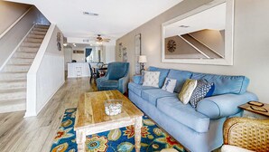 A living room with a blue sofa, wooden coffee table, and a colorful rug. A staircase leads to another room. - Newly renovated two-story waterfront condo with screened porch, pool, & tennis (Folly Beach)