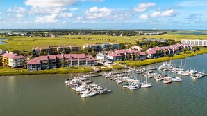 A marina with multiple boats docked, surrounded by buildings with red roofs, and a river in the foreground. - Newly renovated two-story waterfront condo with screened porch, pool, & tennis (Folly Beach)