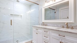 Un baño con ducha de vidrio, un espejo grande y una encimera de mármol.