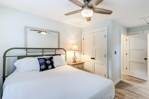 A bedroom with a bed, a nightstand with a lamp, a ceiling fan, a wardrobe, and a door.