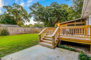 A wooden deck with a staircase leading to a covered area, surrounded by a wooden fence and lush greenery.
