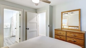 Un dormitorio con cama, cómoda de madera, ventilador de techo y espejo en la pared.