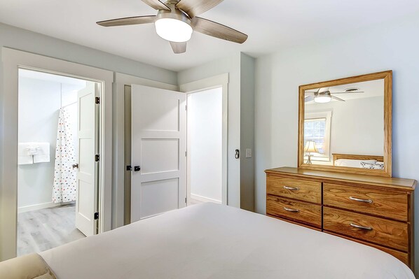 A bedroom with a bed, a wooden dresser, a ceiling fan, and a mirror on the wall.