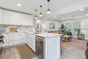 Uma cozinha moderna com armários brancos, bancada de mármore e iluminação pendente.