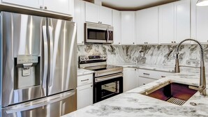 Una cocina moderna con electrodomésticos de acero inoxidable, armarios blancos y encimera de mármol.