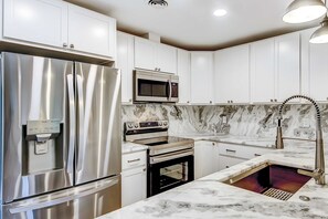 A modern kitchen with stainless steel appliances, white cabinets, and a marble countertop.