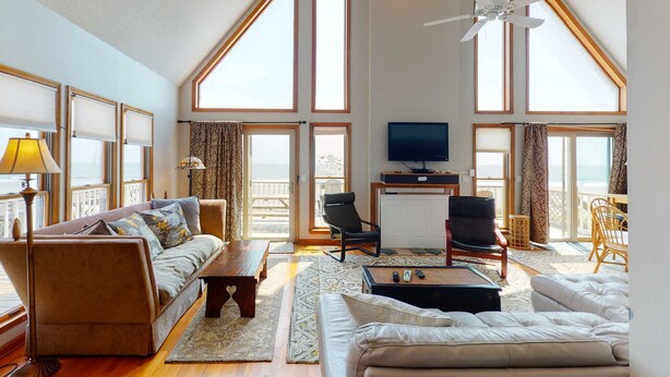 A spacious living room with a high ceiling, large windows, a ceiling fan, a TV, and a balcony. - Oceanfront home with stunning ocean views, central AC, and private W/D (Folly Beach)