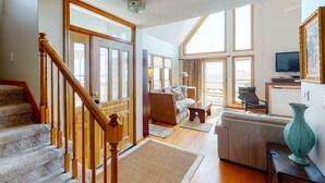 A spacious living area with a staircase, a sofa set, a television, and a large window providing natural light. - Oceanfront home with stunning ocean views, central AC, and private W/D (Folly Beach)