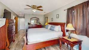 A bedroom with a wooden bed, a ceiling fan, a dresser, a television, and a nightstand with a lamp.